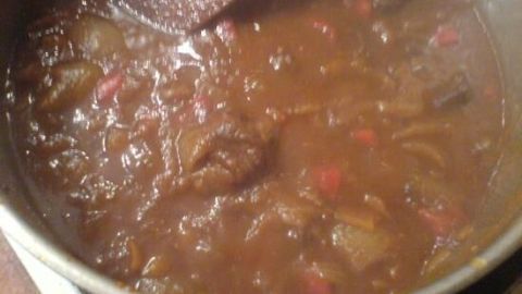 Ein Topf mit Gulasch köchelt, mit sichtbaren Fleischstücken und Paprika, umgeben von einer dampfenden, dicken Sauce.