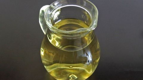 Ein transparentes Glasgefäß mit goldenem Öl steht auf einem dunklen Tisch, bereit zur Verwendung bei Dammriss-Beschwerden.