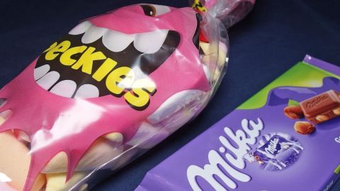 Eine Tüte mit bunten Quengelwaren steht neben einer Tafel Milka-Schokolade auf einem dunklen Untergrund.