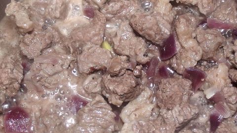 Gulasch aus zartem Rindfleisch kocht in einer Pfanne, umgeben von feinen Zwiebelstücken für den authentischen Geschmack.