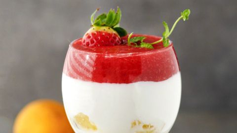Ein elegantes Glas mit Zitronenquark, belegt mit roter Beerensauce und frischen Erdbeeren, steht auf einem silbernen Teller.