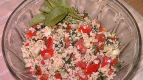 Ein Bulgursalat mit Tomaten, Gurken und Kräutern in einer Glasschüssel, garniert mit frischen Salatblättern auf einem Tuch.