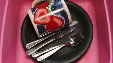 Ein bunten Becher und Besteck befinden sich auf einem tiefen Teller in einer Spüle, bereit zum Geschirr sammeln und spülen.