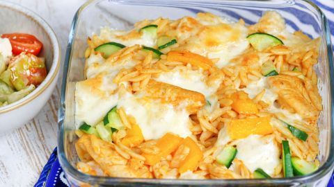 Ein Auflauf mit Nudeln, Hühnchen und Gemüse wird goldbraun überbacken in einer Glasform serviert, daneben ein Salat.