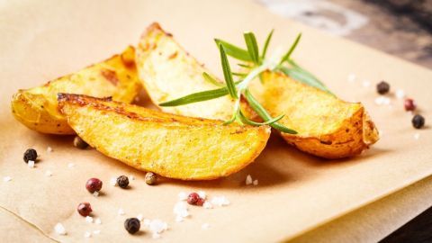 Knusprige Kartoffelspalten liegen dekorativ auf braunem Papier, garniert mit Kräutern und umgeben von buntem Pfeffer.