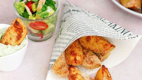 Knusprige Kartoffelecken liegen in einem Papierbecher, daneben eine kleine Schüssel mit Dip und ein gemischter Salat.