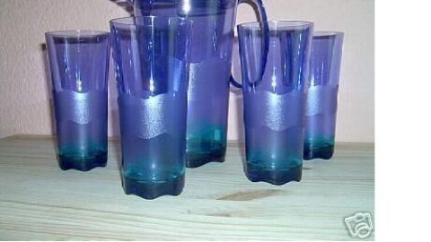 Ein blauer Krug steht neben vier gleichfarbigen Gläsern auf einem Tisch, bereit für gesundes Trinken an einem heißen Sommertag.