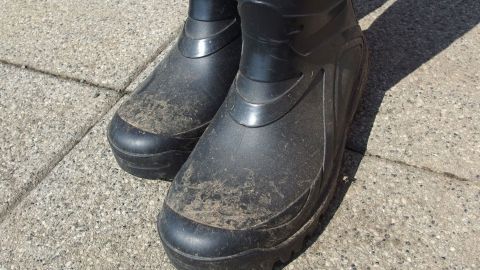 Ako Pads eignen sich hervorragend zum Reinigen von Gummistiefeln. Schwarze Gummistiefel stehen auf einem grauen Gehweg und sind mit Schmutzflecken verunreinigt, bereit zum Säubern.
