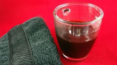 Ein Glas mit schwarzem Tee steht neben einem dunkelgrünen Tuch auf einem roten Hintergrund, bereit zum Färben von Stoff.