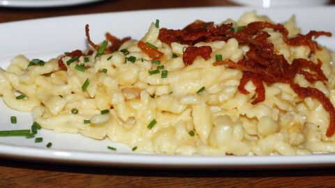 Schwäbische Käsespätzle sind auf einem Teller angerichtet, garniert mit Röstzwiebeln und frischen Kräutern in einer rustikalen Umgebung.