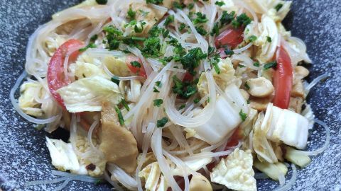 Ein bunter Glasnudelsalat mit dünnen Nudeln, Hähnchenstücken und frischem Gemüse in einer dekorativen Schale.