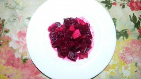 Ein farbenfroher Rote Beete Gurkensalat liegt auf einem weißen Teller und hebt sich von einem blumigen Tischdecke ab.
