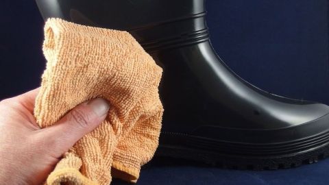 Ein schwarzer Gummistiefel wird mit einem orangefarbenen Tuch gereinigt, um die Haltbarkeit zu erhöhen.