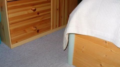 Ein Bett mit scharfen Kanten steht in einem Raum, w&auml;hrend eine Decke sanft &uuml;ber die Kante h&auml;ngt, um blaue Flecken zu vermeiden.