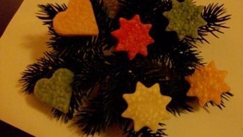 Bunte Wachsfiguren in Herz- und Sternform liegen auf einem Tannenzweig und schaffen eine festliche Weihnachtsstimmung.