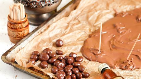 Schokoladenüberzogene Rumrosinen liegen auf einem Backblech, umgeben von flüssiger Schokolade und Dekorationsmaterialien.