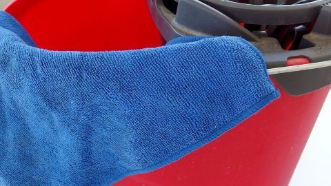 Ein blauer Lappen hängt über einem roten Eimer, während er zum Reinigen genutzt wird, um muffige Wäsche zu befreien.