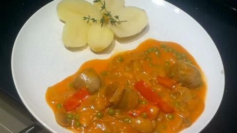 Auf einem weißen Teller liegt ein würziges Dänisches Bratwurstgericht mit buntem Gemüse und einer Blumenkartoffel-Beilage.