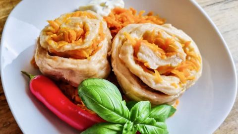 Rollen aus Strudelteig, gefüllt mit Karotten, liegen auf einem weißen Teller neben Chili und frischem Basilikum.