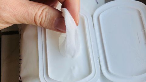 Eine Hand greift nach einem Babyfeuchttuch aus einer geöffneten Packung, um es zu verwenden.