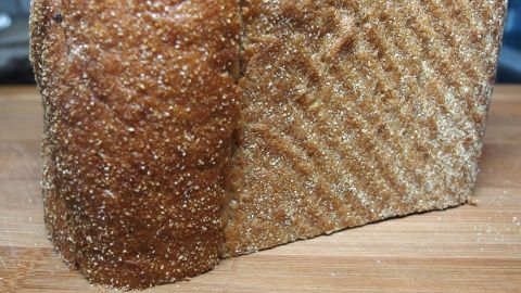 Ein angeschnittenes Brot liegt auf einem Holzbrett, wobei die Kruste sichtbar ist. Die Umgebung wirkt küchentechnisch.