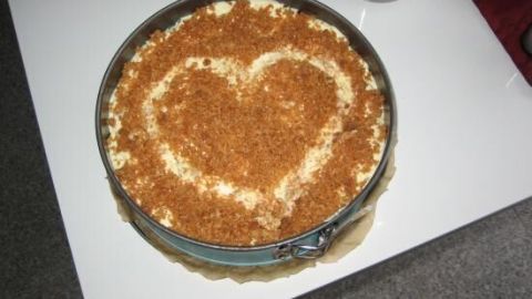Ein leckerer Sägespänekuchen mit einem herzförmigen Muster aus Bröseln, auf einem weißen Tisch serviert.