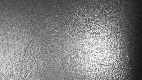 Ein glattes, schwarzes Ledermöbelstück liegt im Fokus, es reflektiert leicht das Licht in einem neutralen Raum.