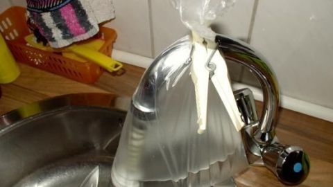 Ein Wasserhahn mit einem durchsichtigen Beutel gefüllt mit einer Reinigungslösung hängt über einer Spüle.