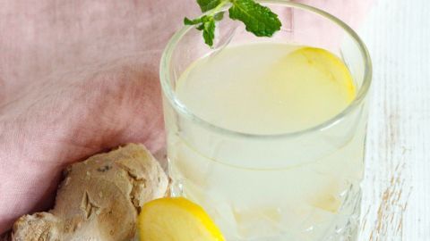 Ein Glas erfrischende Ingwer-Limonade steht auf einem Holztisch, umgeben von frischem Ingwer und einer Zitronenscheibe.