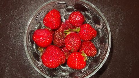 Eine Schüssel voller frischer, roter Erdbeeren liegt auf einem dunklen Tisch, bereit zum genussvollen Verzehr.