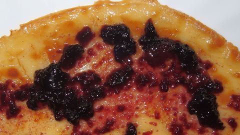 Ein goldbrauner Pfannkuchen belegt mit dunkler Beerenmischung liegt auf einem weißen Teller, bereit zum Servieren.