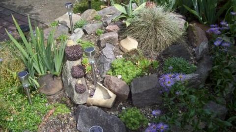 Eine Kräuterspirale mit Hauswurz und Sedum präsentiert sich in einem Garten. Sie wächst zwischen Steinen und Pflanzen.
