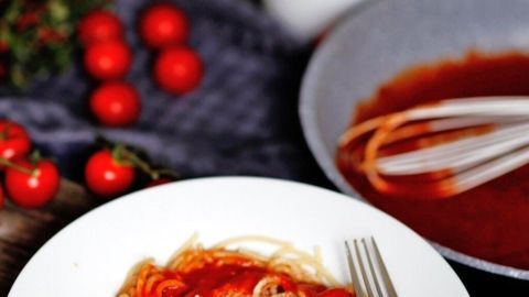 Ein Teller Spaghetti umgeben von frischen Tomaten und einer Schüssel mit roter Tomatencreme auf einem Holztisch.