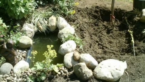Ein Gartenteich aus Mörtelwannen wird von Steinen umgeben, während die Erde um ihn herum bearbeitet wird.