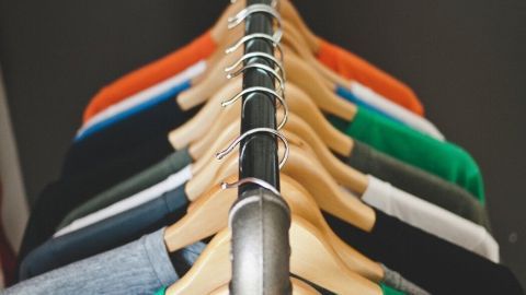 Bunte T-Shirts hängen ordentlich an einem Kleiderständer, während ein großer Kalender an der Wand im Hintergrund sichtbar ist.