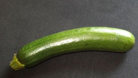 Ein frischer Zucchini liegt auf einer dunklen Oberfläche, bereit zum Andünsten und anschließenden Einfrieren.