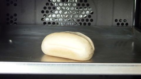 Ein Brötchen liegt auf einem Blech im Backofen und wird zum Fertigbacken erwärmt, um goldbraun und knusprig zu werden.