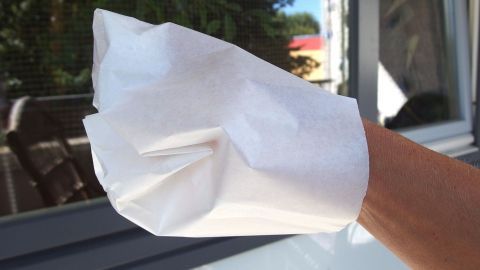 Eine Hand trägt einen zerknautschten Butterbrotbeutel und reinigt damit ein Fenster im Freien.