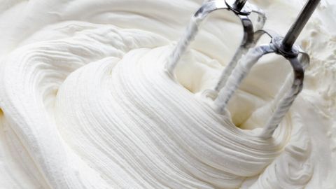 Schlagsahne wird mit einem Handmixer geschlagen, der in eine schaumige, weiße Masse eintaucht.