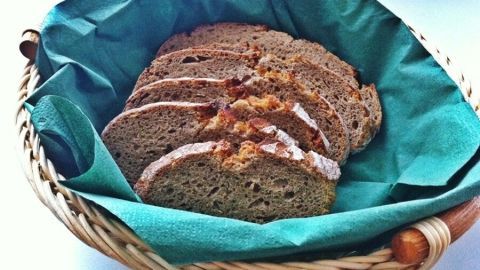 Eine geflochtene Korb mit frischem, geschnittenem Brot liegt auf grünem Tuch. Es wirkt einladend und hausgemacht.