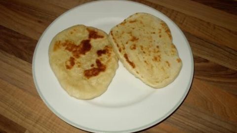 Zwei gebräunte Naan-Brote liegen auf einem weißen Teller, der auf einem Holztisch steht.