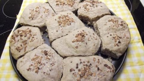 Knusprige Weizenvollkorn-Brötchen liegen auf einem schwarzen Blech, umgeben von einem gelben, karierten Tuch.