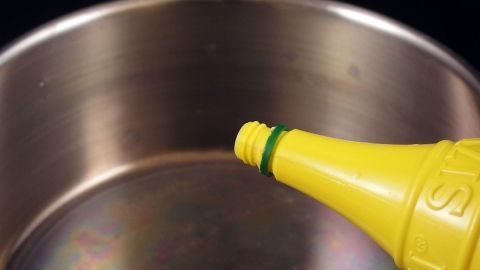 Ein Kochtopf aus Edelstahl wird gereinigt, während Flüssigkeit aus einer gelben Zitronenflasche eingegossen wird.