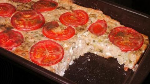 Ein Kartoffel-Schafskäse-Auflauf liegt in einer dunklen Backform und ist mit rohen Tomatenscheiben dekoriert.