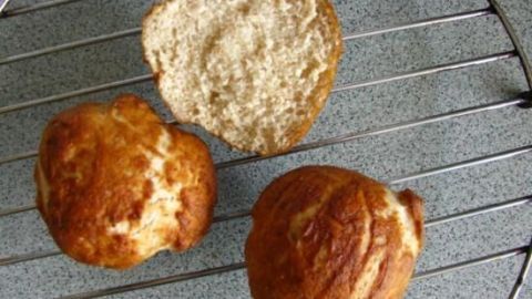 Drei frisch gebackene Laugenbrötchen liegen auf einem Abkühlgitter, während sie abkühlen und golden glänzen.