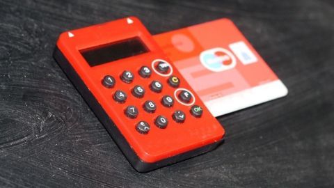 Ein roter TAN-Generator liegt auf einem dunklen Tisch neben einer Bankkarte, bereit zur Nutzung für Online-Banking.