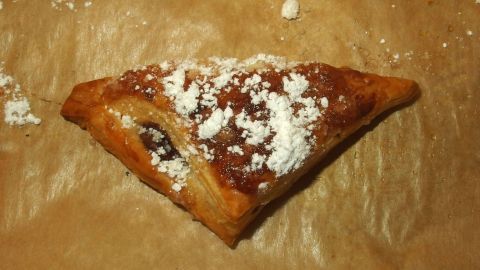 Ein herzhaftes Blätterteig-Häppchen mit Nutella liegt auf Backpapier, bestreut mit Puderzucker in einer warmen Küche.