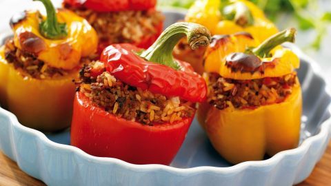 Bunte gefüllte Paprika stehen in einer Schüssel, gefüllt mit würzigem Reis und Hackfleisch, umgeben von frischem Grün.
