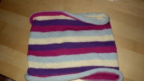 Ein gestricktes, bunt gestreiftes Stück liegt flach auf einem Holztisch.