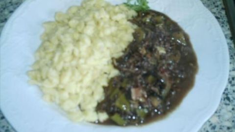 Ein Teller mit Ragout de boeuf haché au vin rouge, serviert mit Spätzle, auf einer weißen Unterlage in einer Küche.